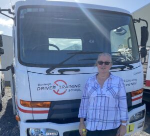 Female trainee truck driver standing in front of a truck