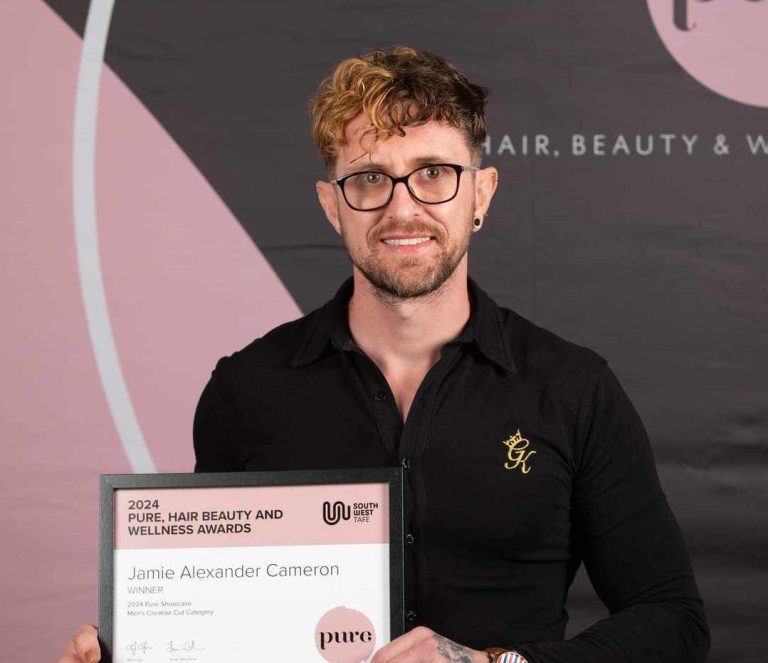 A person with short, curly hair, glasses, and a beard is proudly holding an award certificate. The backdrop displays PURE, Hair Beauty and Wellness Awards. The certificate celebrates Jamie Alexander Cameron from Concept Hair as the Winner for 2024. This achievement was facilitated by BUSY at Work.
